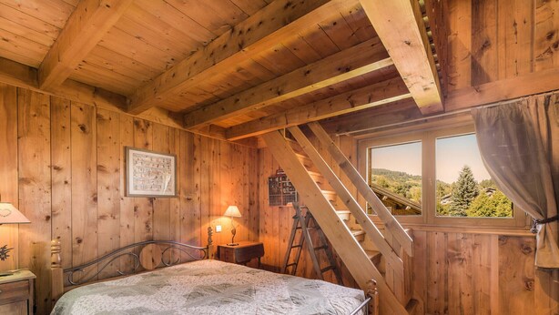 Une chambre dans une cabane en bois, avec un lit, une fenêtre donnant sur un paysage et une échelle.