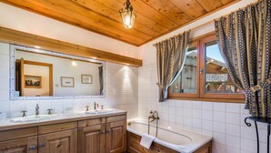 Une salle de bain de style rustique, avec des murs en bois, un grand miroir, deux lavabos, une baignoire et des rideaux à motifs.