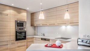 A modern kitchen with wooden cabinets, stainless steel appliances, a central island with bar stools, and pendant lighting.