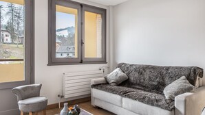 A modern living room with a grey sofa, a grey armchair, and a clear glass coffee table with decorative items.