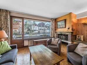 Un salon chaleureux avec un plancher en bois, une cheminée et une grande fenêtre donnant sur l’extérieur.