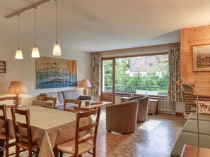 Un coin repas avec des meubles en bois, un tableau accroché au mur et une vue dégagée sur l’extérieur grâce à une grande fenêtre.