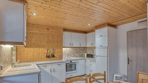 Une cuisine moderne avec un plafond en bois, des armoires blanches, un four encastré et une table à manger avec des chaises.