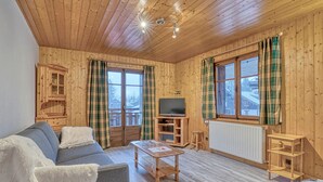 Une cabane en bois chaleureuse, avec un canapé, une petite table, un téléviseur et des rideaux à carreaux.