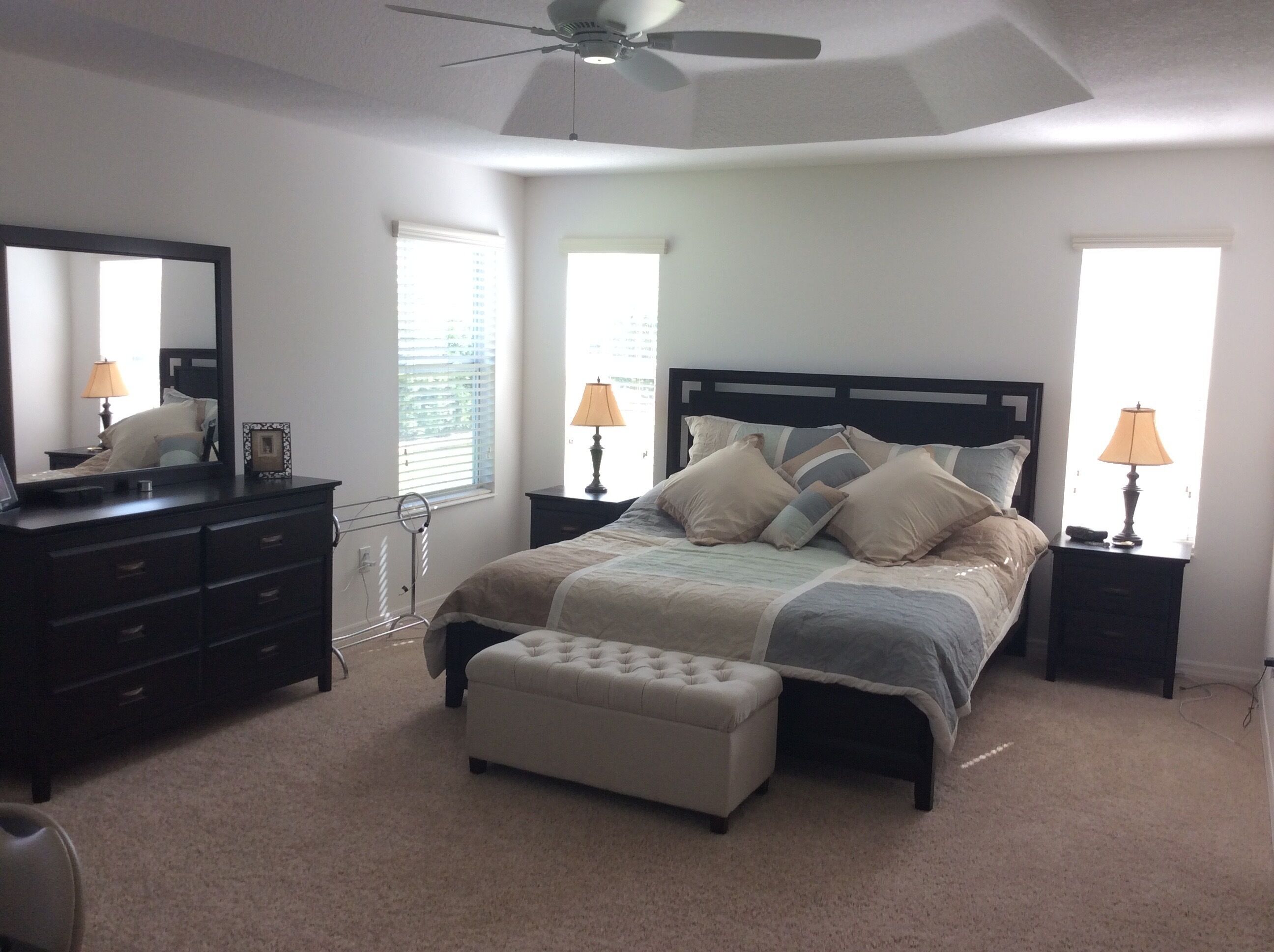 A bedroom with a bed, a dresser, a mirror, two bedside lamps, and a ceiling fan.