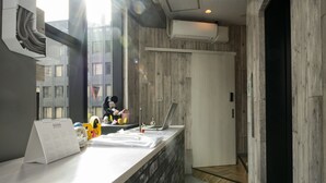 A reception desk with a calendar, a laptop, and a small figurine. There is a window with a view of buildings outside. - bnb+ Kanda - Hostel (Tokyo)
