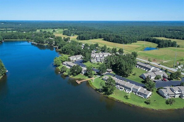 An aerial view of a residential area with houses, a lake, and surrounding greenery.