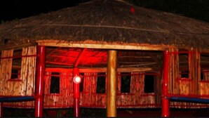 A thatched-roof hut with a red-lit interior, wooden walls, and a central support pillar.