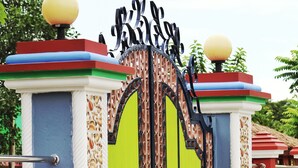 A colorful gate with a green door, decorative pillars, and two spherical finials on top.