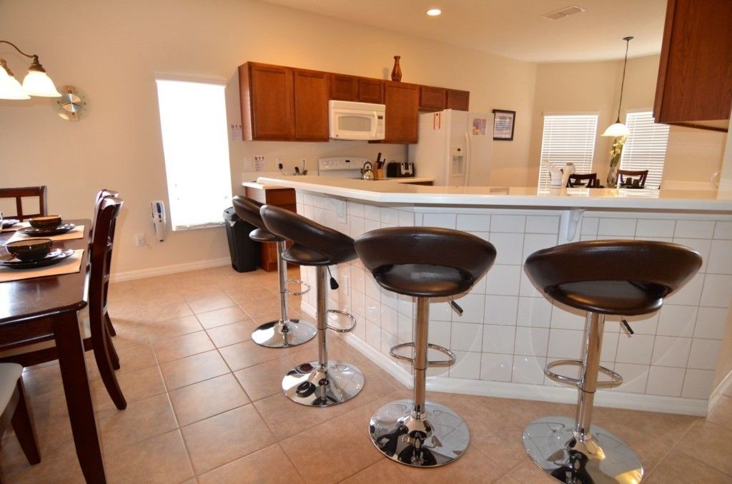 A modern kitchen with wooden cabinets, a white countertop, and three bar stools.
