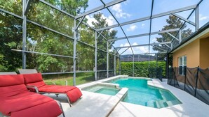 A covered outdoor swimming pool with red lounge chairs, surrounded by glass walls and a view of greenery.
