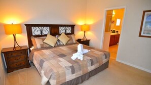 A neatly made bed with a checkered bedspread, two bedside lamps, and a small wooden nightstand with drawers.