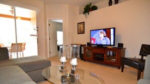 A living room with a glass coffee table, grey sofas, a television, and a wooden cabinet.
