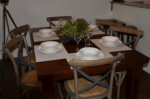 A dining table set for six with white plates, glasses, and a centerpiece of greenery.