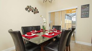 A dining area with a glass table, black chairs, red napkins, and a decorative wall piece.