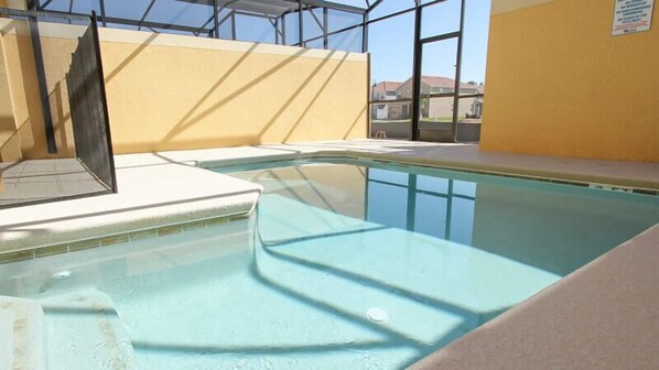 An indoor swimming pool with clear glass walls, a tiled floor, and a yellow wall.