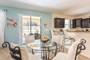 Relax in this inviting space with a dining area and kitchen, featuring a glass-top table and comfortable seating.