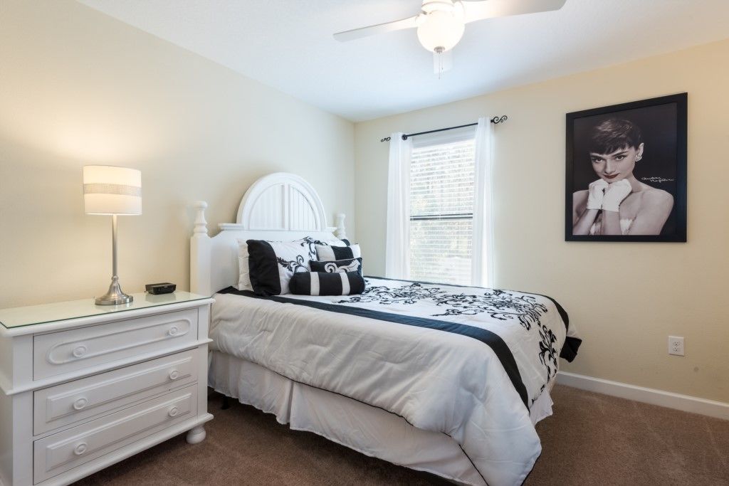 A bedroom with a bed, a dresser, a lamp, a ceiling fan, a window with blinds, and a framed picture on the wall.