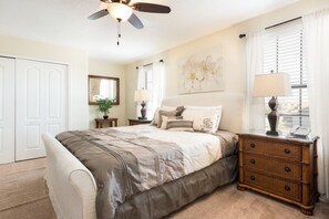 A bedroom with a large bed, a ceiling fan, a nightstand with a lamp, a dresser, and a window with curtains. - Ev239275 - Champions Gate Resort - 6 Bed 5 Baths Villa (Davenport)