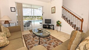 Una sala de estar con una mesa de centro de vidrio, sofás, un televisor y una escalera.