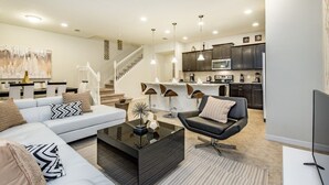 A modern living room with a sofa, armchair, and coffee table, connected to a kitchen with dark cabinets and a microwave. - Ev216592 - Windsor At Westside Resort - 5 Bed 4 Baths Townhome (Kissimmee)