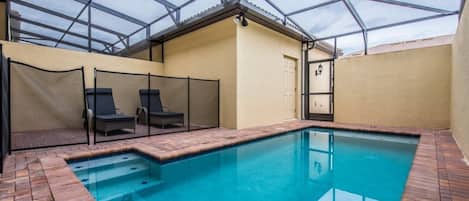 An indoor swimming pool with a glass ceiling, surrounded by lounge chairs and a brick floor.