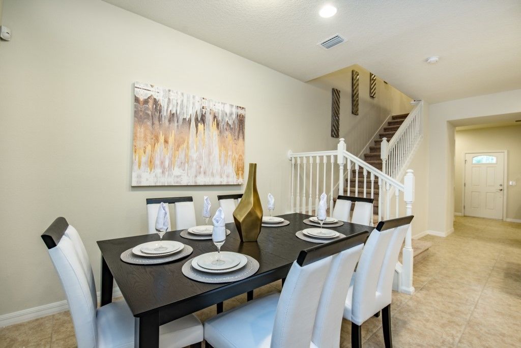 A dining area with a dark wooden table set for four, white upholstered chairs, and a large abstract painting on the wall.