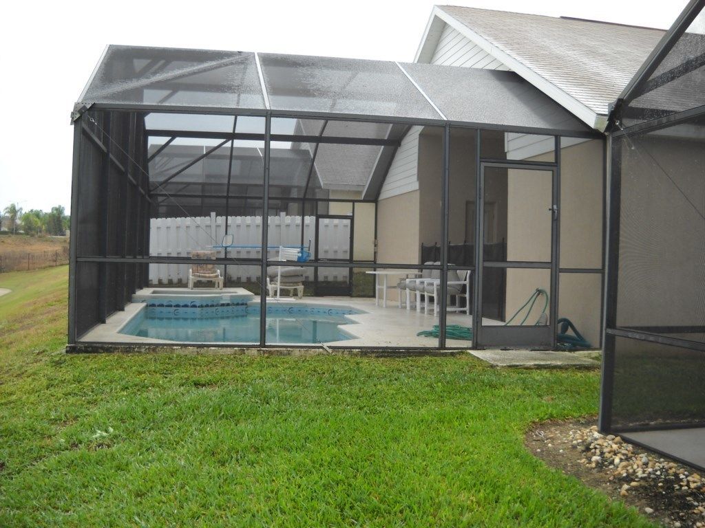 A screened-in patio with a pool, outdoor furniture, and a covered area.