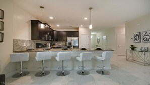 A modern kitchen with dark cabinets, a stainless steel refrigerator, and a central island with bar stools.