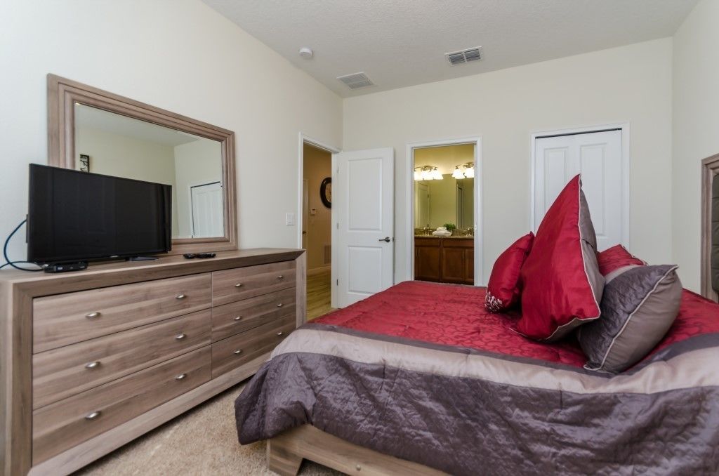 Quarto com uma cama grande, cômoda, televisão e banheiro visível por uma porta aberta.