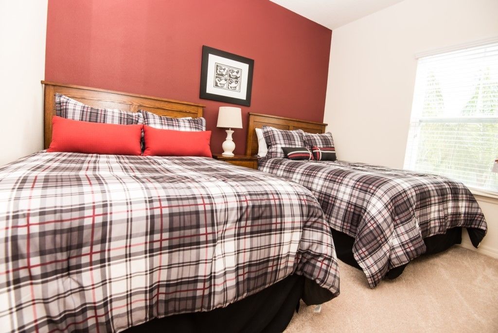 A bedroom with two beds, each with plaid bedding, a red accent pillow, and a framed picture on the wall.