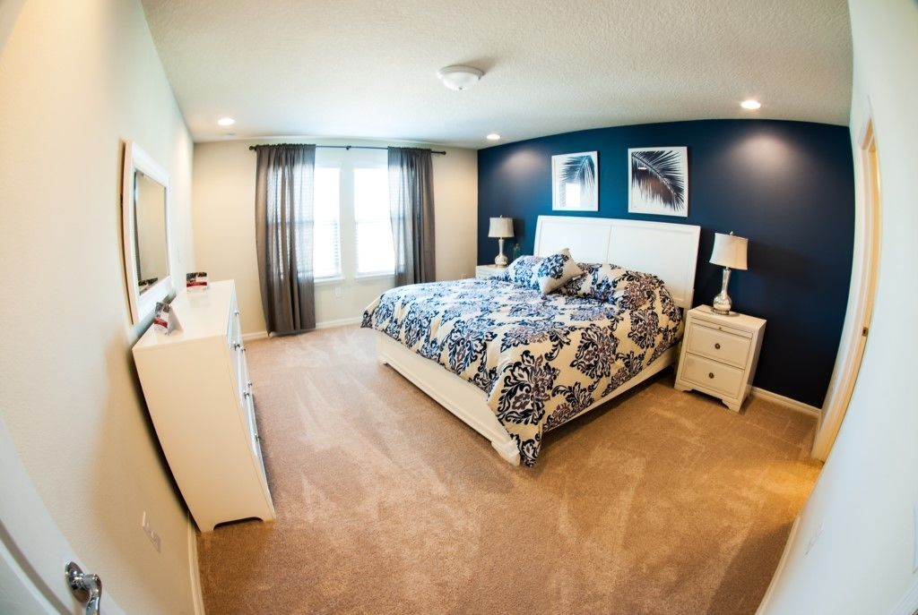 A bedroom with a large bed, a dresser, two bedside tables with lamps, and a window with curtains.