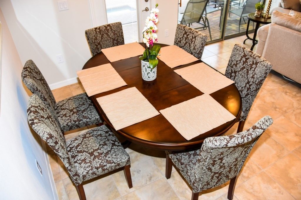 A round dining table with a wooden finish, surrounded by patterned upholstered chairs.