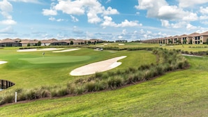 A golf course with bunkers, a putting green, and a clubhouse in the background.