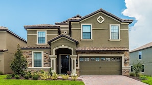 A two-story house with a stone facade, a front entrance with a door, and a garage. - Grhrfd1411 - Champions Gate Resort - 9 Bed 5 Baths House (Davenport)