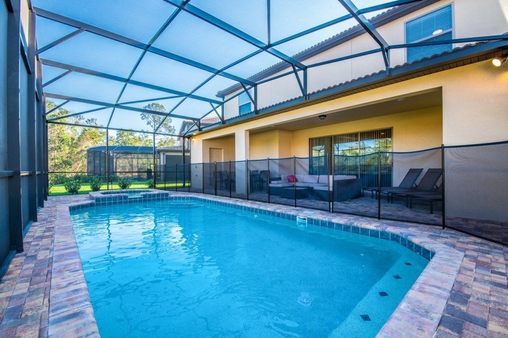 An indoor swimming pool with a glass ceiling, a brick pool edge, and a seating area with a sofa and chairs.