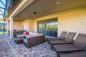 Un patio cubierto con una mesa y sillas de comedor, un sofá con cojines y varias sillas reclinables.