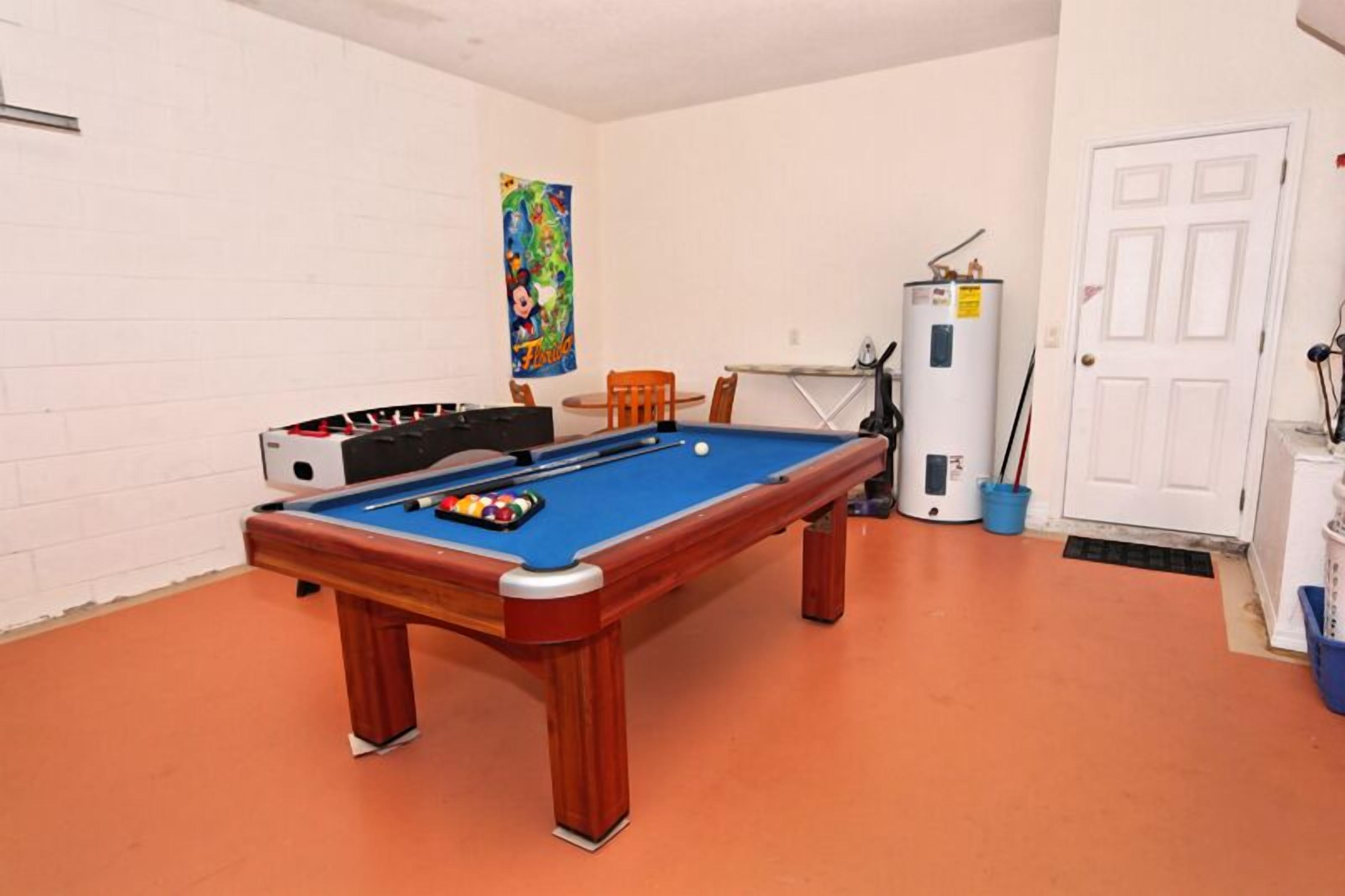 A pool table with a blue felt surface, surrounded by orange walls and a white door.
