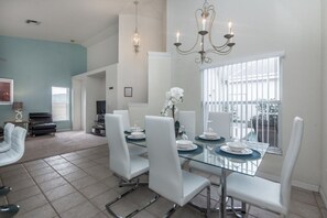 A dining area with a glass table, white chairs, and a chandelier. - Ev215108 - The Abbey at West Haven - 4 Bed 3 Baths Villa (Davenport)