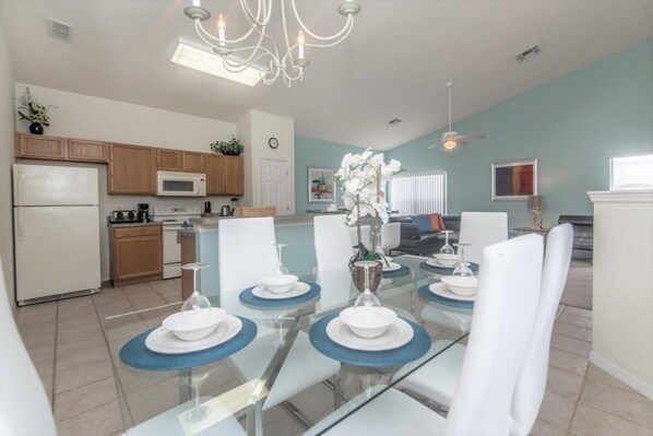 A modern kitchen with wooden cabinets, a microwave, and a dining area with a glass table set for four.