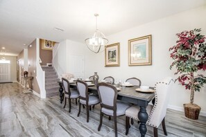A dining area with a wooden table set for six, surrounded by chairs. A staircase is visible in the background leading to another room. - Ev242169 - Champions Gate Resort - 8 Bed 5 Baths Villa (Davenport)