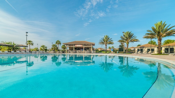 Ein großer, klarer Pool mit Liegestühlen und Palmen, umgeben von Gebäuden mit einer überdachten Terrasse.