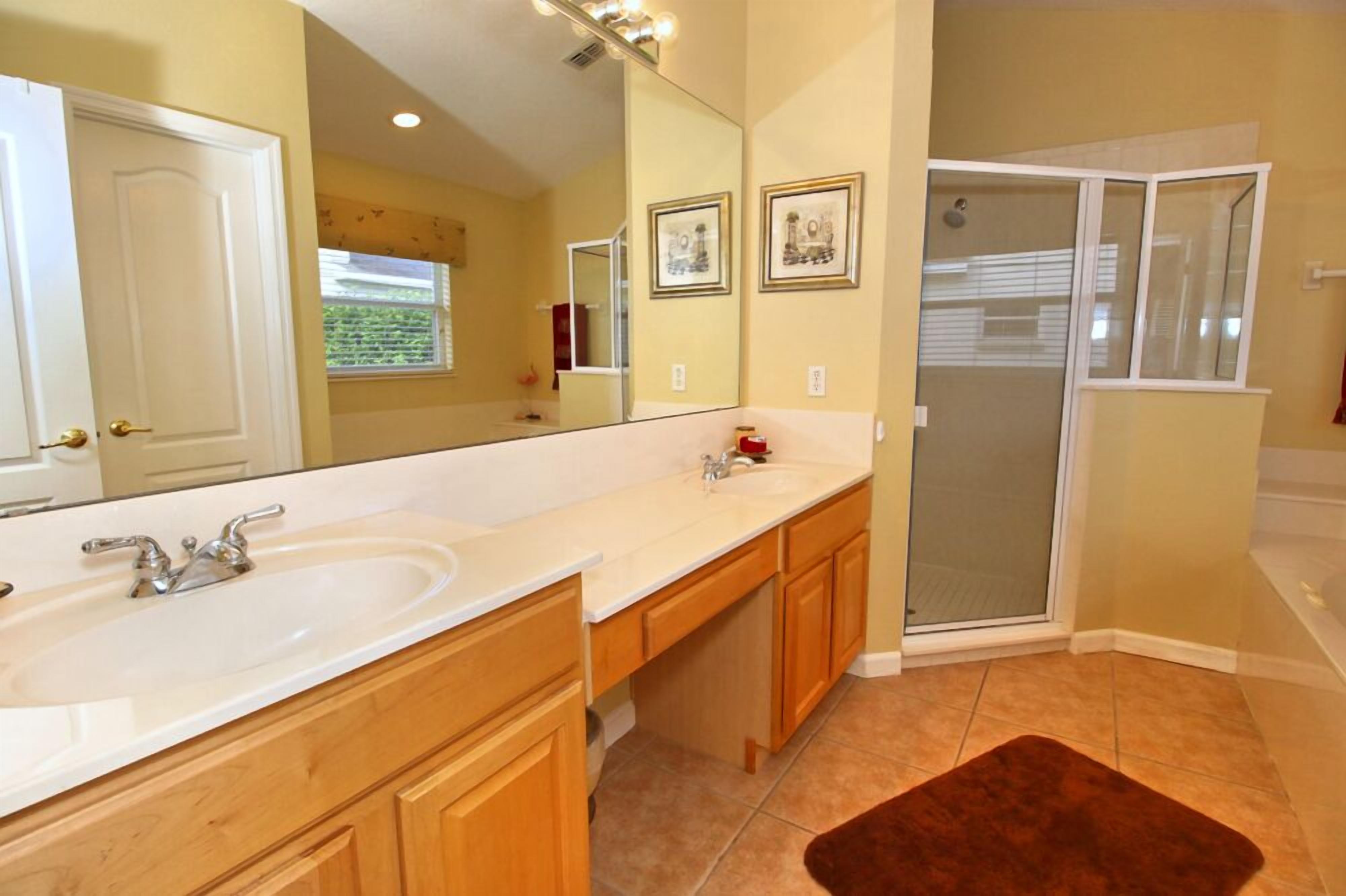 A bathroom with two sinks, a large mirror, wooden cabinets, a shower with glass doors, and a brown rug.