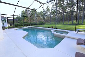 Une piscine avec un jacuzzi, le tout entouré d’une structure en verre offrant une vue sur une zone boisée.