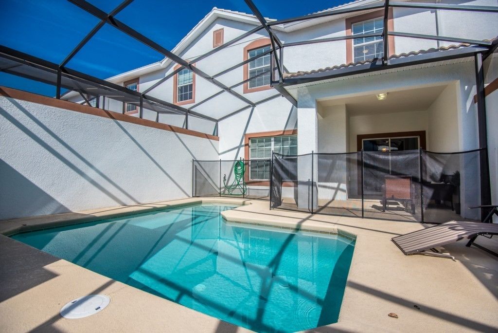 A swimming pool with a glass enclosure, a covered patio area, and a building with a white facade and red trim.