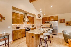 A modern kitchen with wooden cabinets, a central island with bar stools, a stainless steel refrigerator, and a hanging light fixture. - River Run Townhome RR84 - RVJR by RedAwning (Keystone)