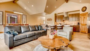 A spacious living room with a leather sofa, a wooden coffee table, and a dining area with a kitchen in the background. - River Run Townhome RR84 - RVJR by RedAwning (Keystone)
