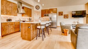 A modern kitchen with wooden cabinets, a central island with stools, stainless steel appliances, and a flat-screen TV mounted on the wall. - River Run Townhome RR84 - RVJR by RedAwning (Keystone)