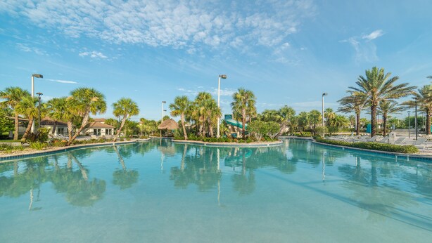 A clear swimming pool surrounded by palm trees and lounge chairs, with a clear sky above.