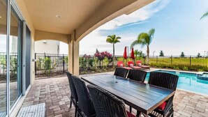 Eine überdachte Terrasse mit Pool, Gartenmöbeln und Blick auf den Poolbereich.